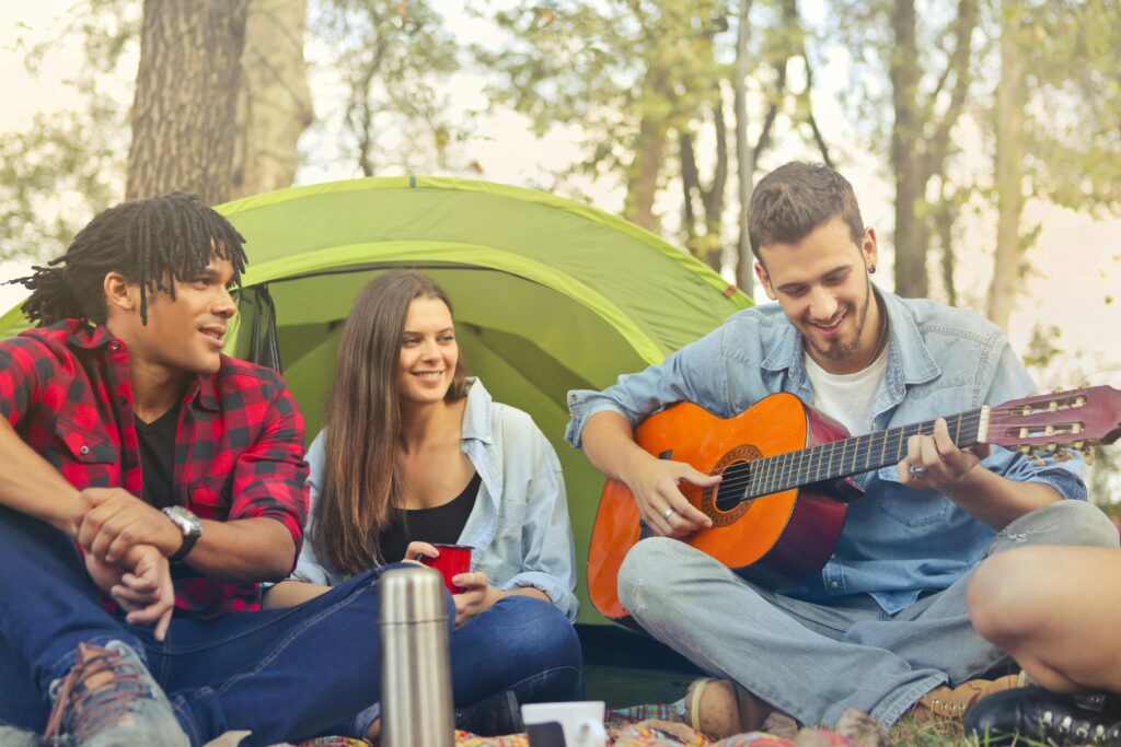 Group of friends having fun and playing guitar while camping in summer.